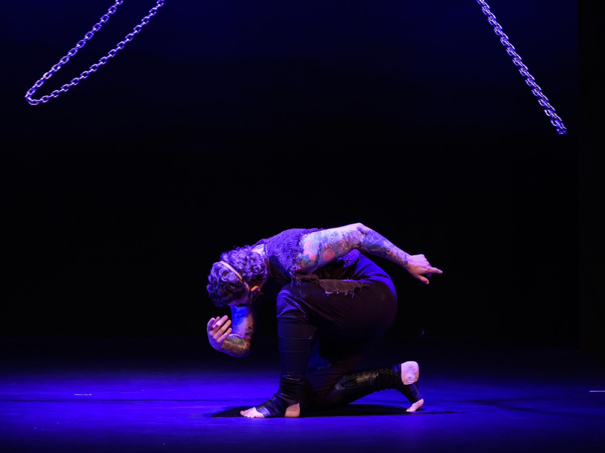 A performance photo of Alec kneeling beneath circling chains.
